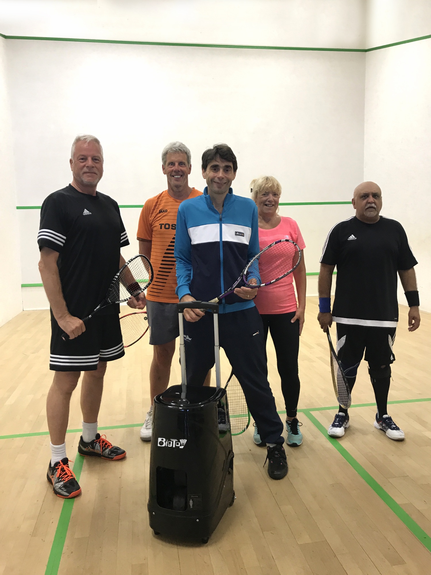 Club players gathered around a squash ball machine